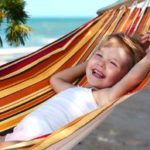 Ferienzeiten - ein lachendes Kind am Strand in einer Hängematte