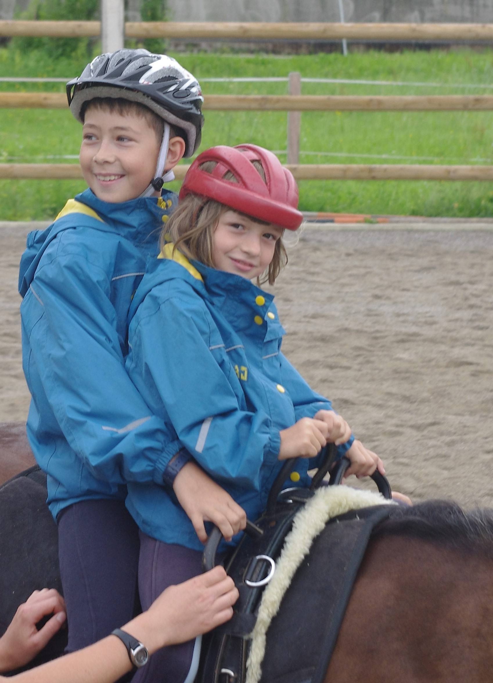 Zwei Kinder sitzen bei der heilpädagogischen Ferienmaßnahme zusammen auf einem Pferd