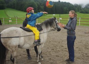 Ein Mädchen und ihre Reittherapeutin spielen Ball auf dem Pferd