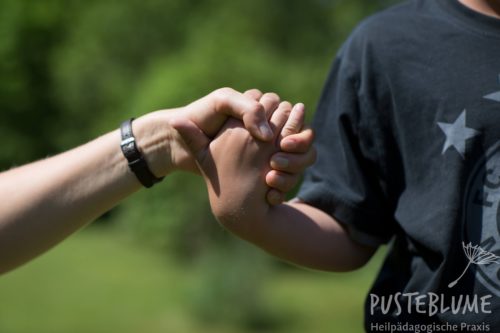 Eine Heilpädagogin reicht einem Jungen die Hand. 