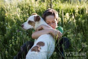 Ein Junge umarmt einen Hund und schließt dabei in tiefer Zuneigung die Augen.