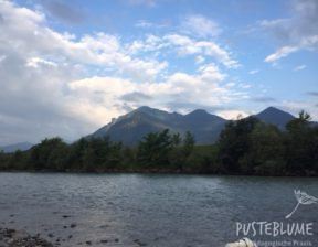 Im Vordergrund fließt die Tiroler Ache. Im Hintergrund sieht man die Berge und blauen Himmel.